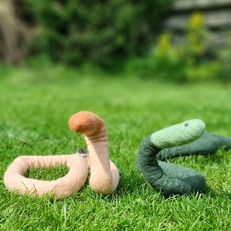 Trivet in wool in the shape of a snake lying together in the grass in different colors.