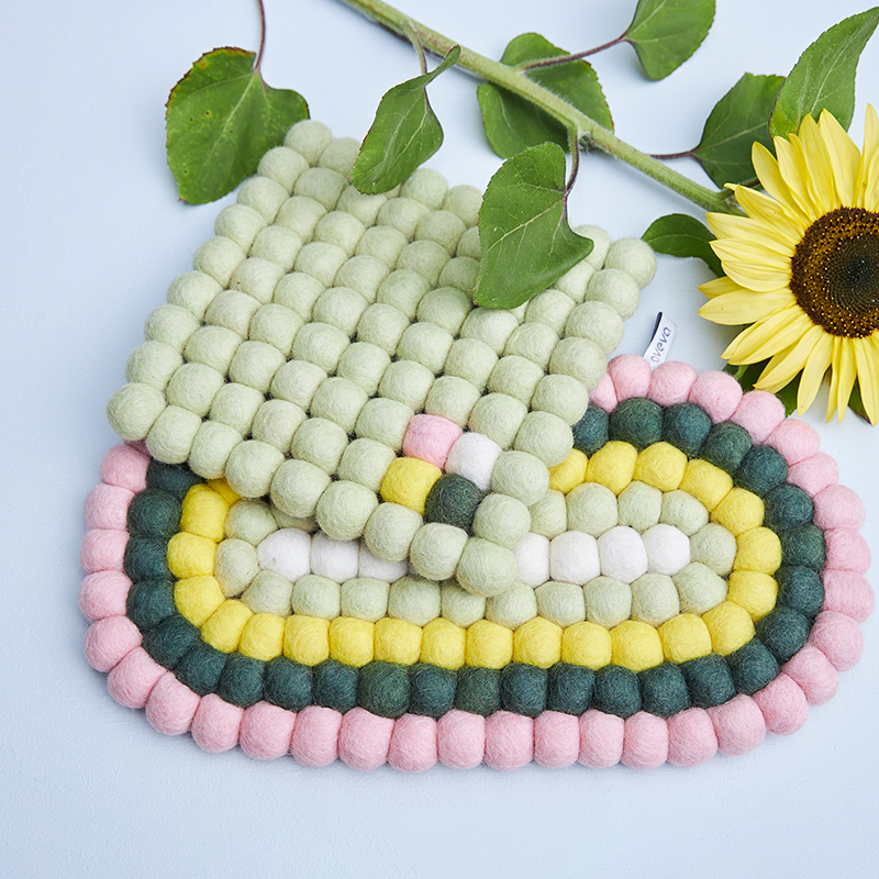 Square and oval trivet in different pastel colors with a sunflower lying next to it.
