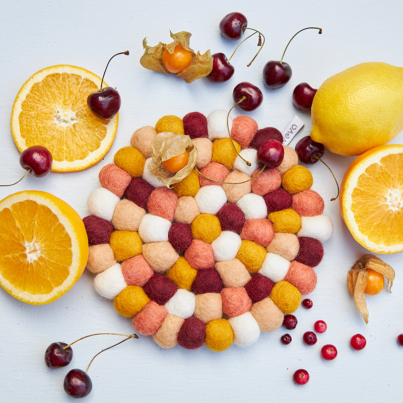 Round trivet in mixed colors with placed citrus fruits next to the trivet.