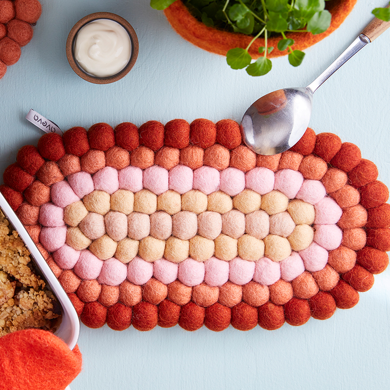 Ovalt grytunderlägg i 100% ull, med färger i rosa, rost, terracotta och beige.