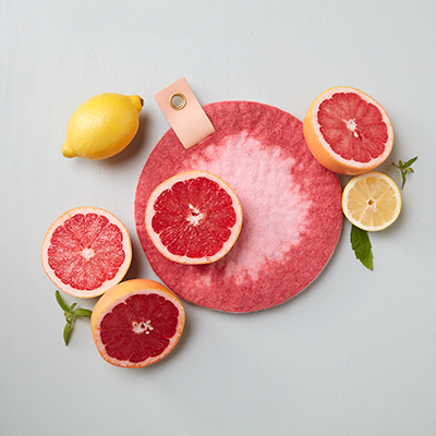 Rund grytunderlägg i ombre med citrusfrukter som ligger bredvid.