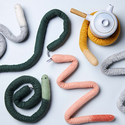 Trivet in wool in the shape of a snake lying together in different colors.