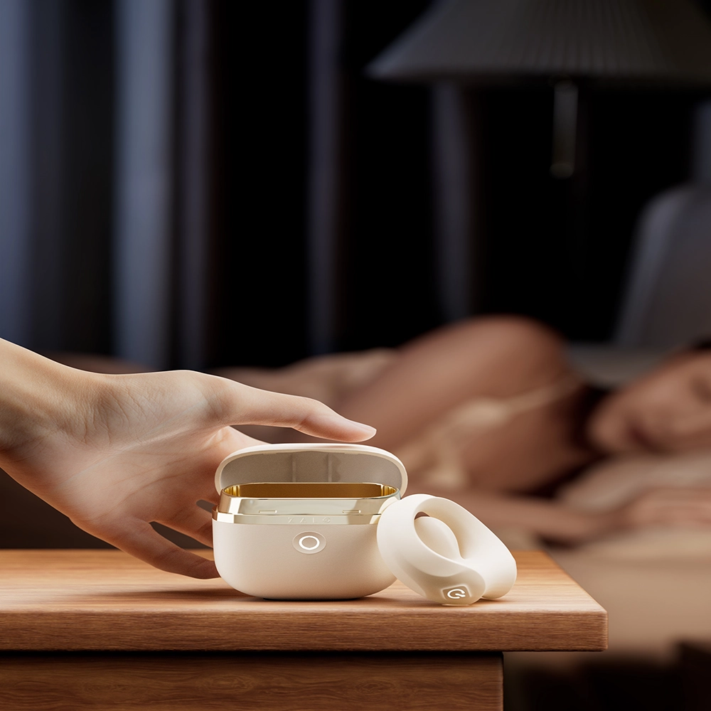 Eine Männerhand hält einen weißen APIS Penisring von ZALO, Frau liegt sinnlich auf dem Bett – exklusiv bei Chambers of Love.