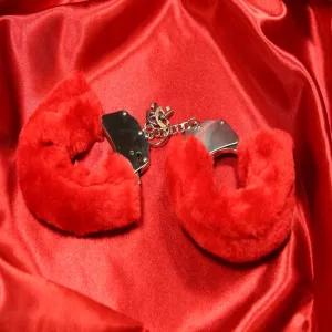 Red fluffy handcuffs with removable faux fur from Chambers of Love on a red background.