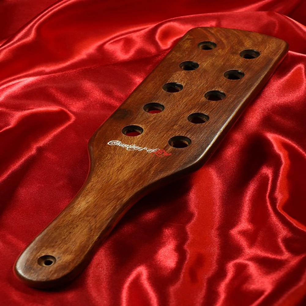 Chambers of Love exklusiv Sheesham träpaddel i storlek M. De 10 hålen i bladet minskar luftmotståndet och ger en hårdare, mer direkt träff – perfekt för kraftfull impact play och eleganta sessioner.