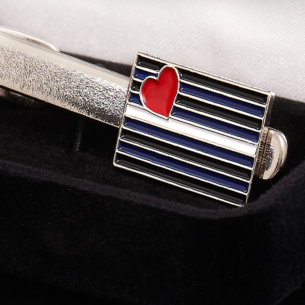 Närbild på slipshållare i blankpolerad metall med läder-flagga, där detaljer och färger framhävs. Elegant accessoar från Chambers of Love.