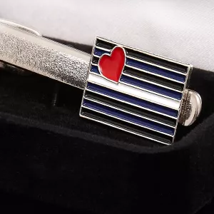 Close-up of polished metal tie clip with leather flag, highlighting details and colors. Elegant accessory from Chambers of Love.