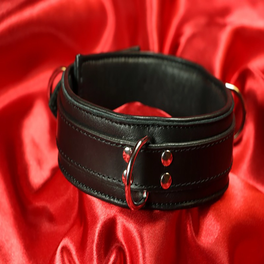 Detaljbild på smalare vadderat BDSM-halsband med 3 D-ringar från Chambers of Love, fotograferad mot röd bakgrund. Elegant och exklusiv design.