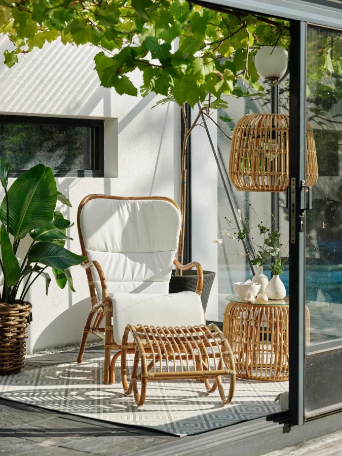 Vallda fåtölj med hög rygg från Brafab ihop med dyna, fotpall och bord i en miljö.