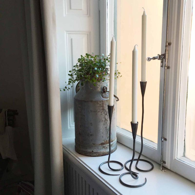 två stycken ljusstakar i svart smide står i ett fönster