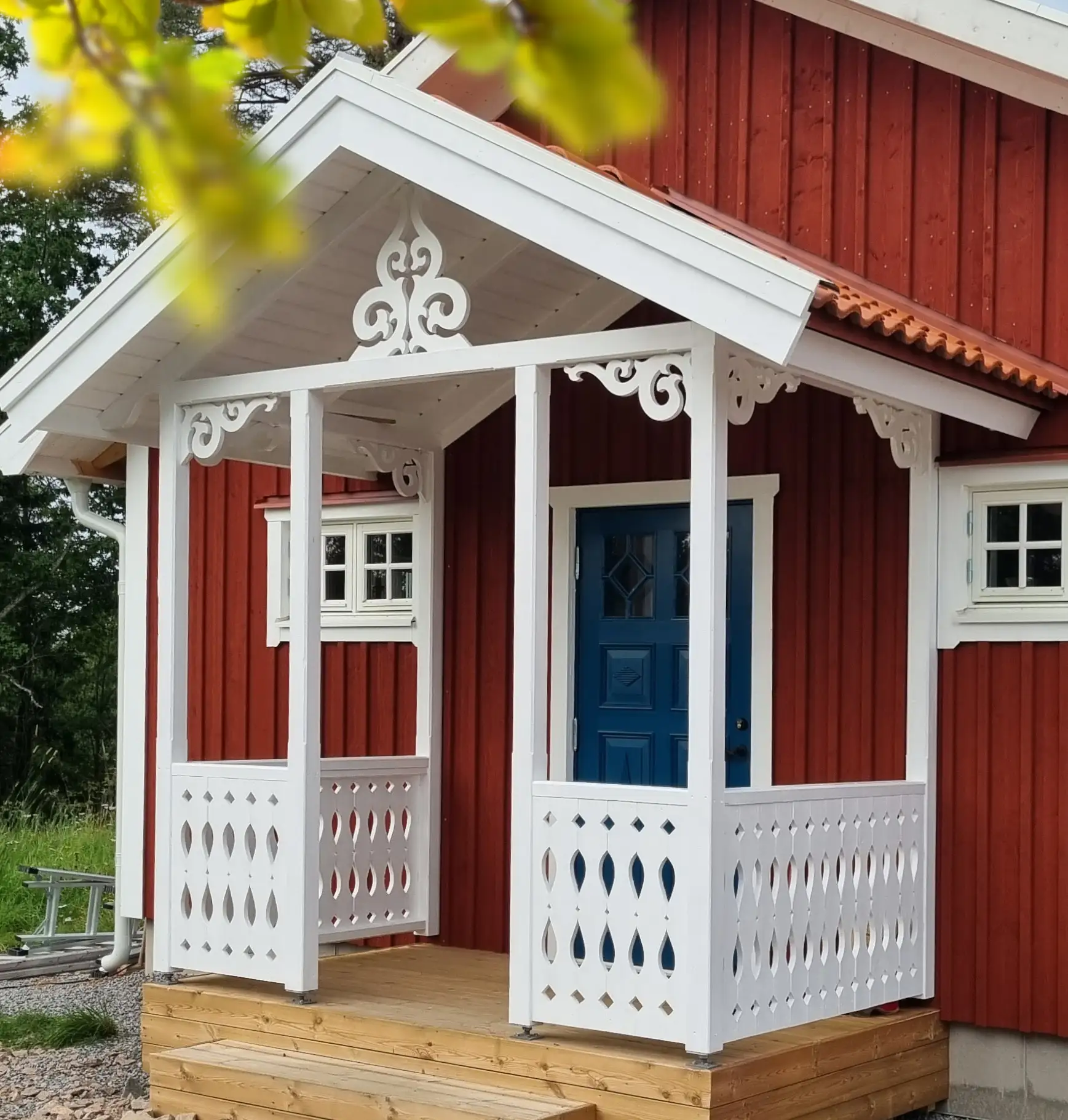 En röd veranda, farstukvist, farstubro med vitt räcke och vita pelare i svensk stil med dekorationer och konsoler i gammaldags stil och allmoge.