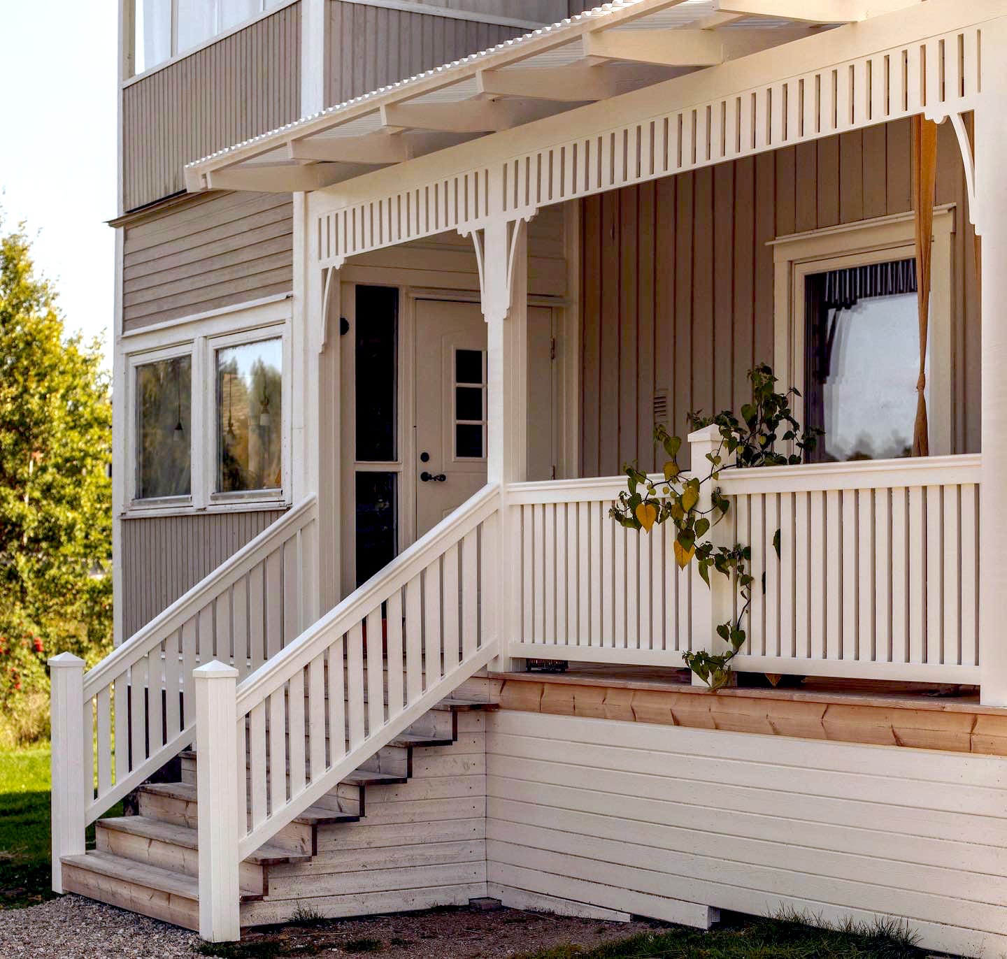 A grey Swedish house with Victorian brackets on a white painted porch