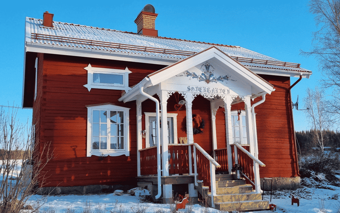 A red Swedish house with ornaments and decorative brackets.