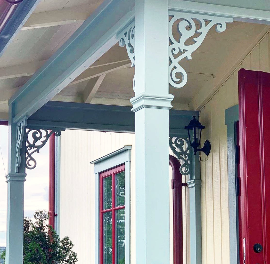 A beautiful yellow Swedish porch with grey pillars and decorative ornaments and wooden brackets.