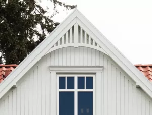 Gable pediment 020 - A white house with decorative wooden victorian millwork as house decoration for roof and gable end. The top frame is mounted behind the eaves.