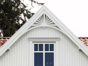 Gable pediment 040 - A white house with decorative wooden victorian millwork as house decoration for roof and gable end. The top frame is mounted behind the eaves.