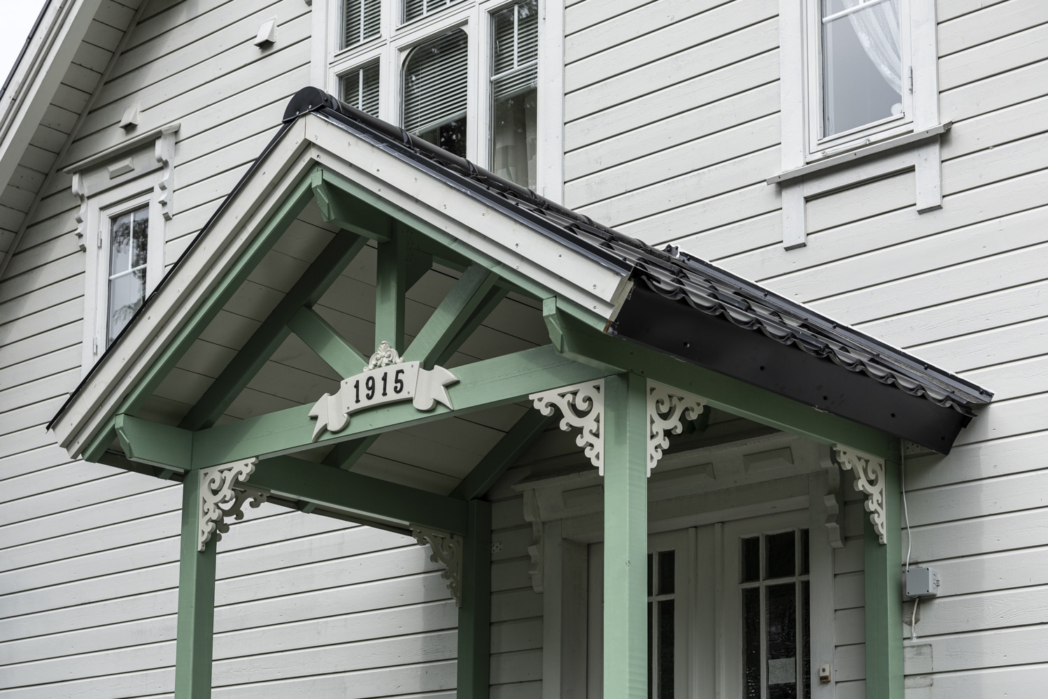 A grey house with a green porch decorated with bracket 001. Classic wooden corbels with ornaments for porch, portico and veranda.