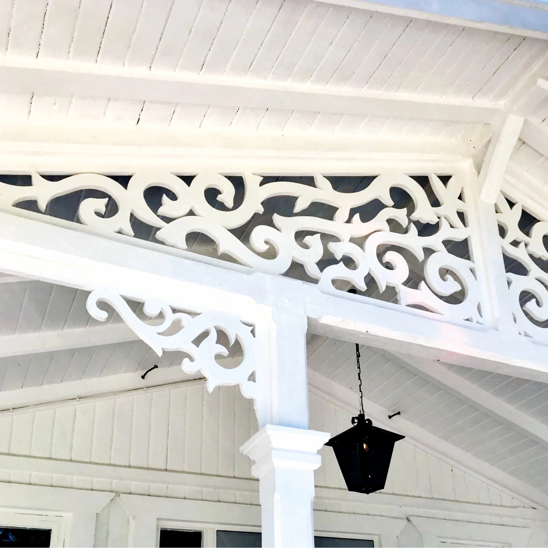 A white porch with carpentry joy, wooden brackets mounted outdoors adjacent to posts, and wooden ornaments in an old style inspired by the turn of the century, the 19th century.
