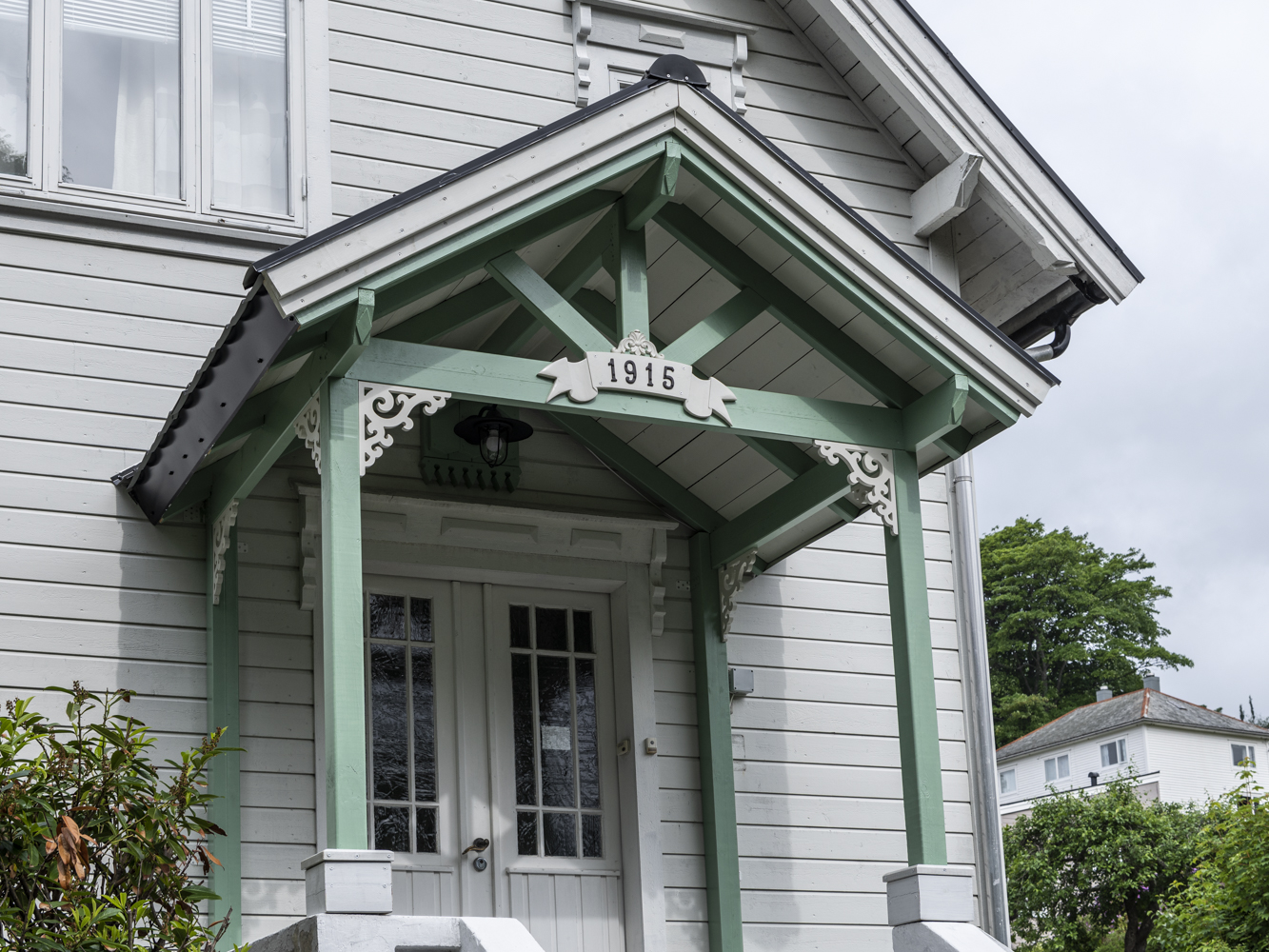 A grey house with a green porch decorated with bracket 001. Classic wooden corbels with ornaments for porch, portico and veranda.