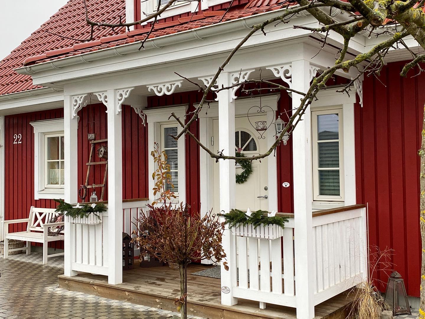 Ein altes rotes schwedisches Haus mit einer weißen Eingangsveranda und dekorativen Holzkonsolen für den Außenbereich. Eine Veranda, inspiriert vom Jahrhundertwechsel und dem 19. Jahrhundert - Gaveldekor.