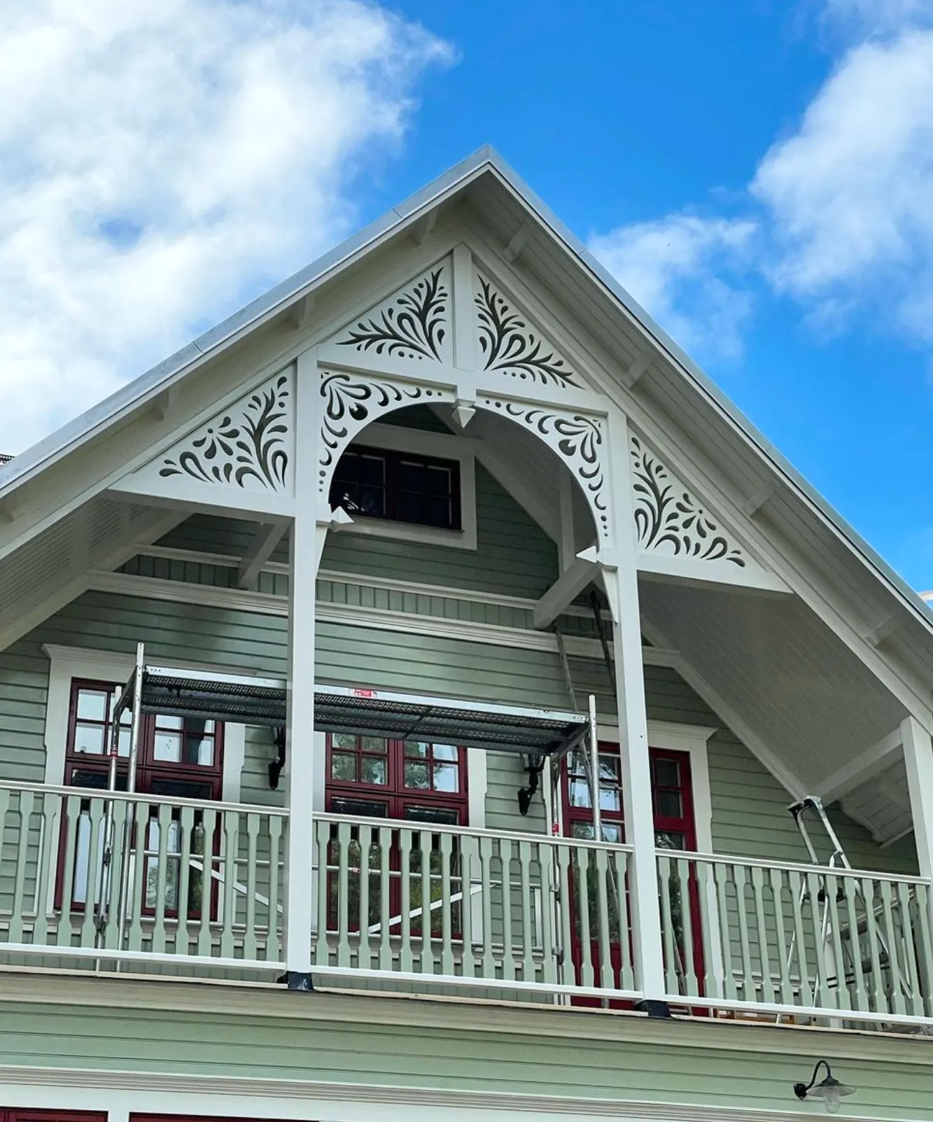 A green house with a porch and a lot of house decoration - wooden brackets - A beautiful turn-of-the-century house inspired by red windows from the turn of the century and 19th-century style - Gaveldekor.