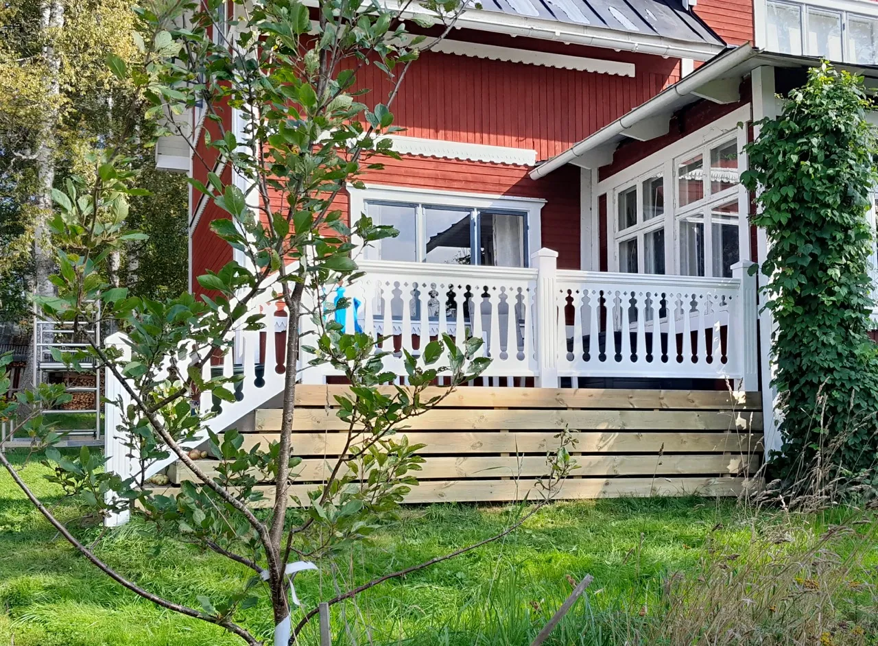 Ein rotes Haus mit einem weißen Holzzaun auf der Veranda und Terrasse im altmodischen Stil mit schwedischer Hausdekoration. Geländerspindeln inspiriert vom 19. Jahrhundert und der Jahrhundertwende - Gaveldekor.