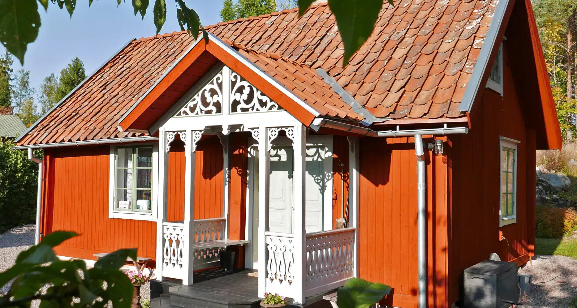 Red wooden house with intricate decorative woodwork, wooden railing, house decor, and traditional porch.