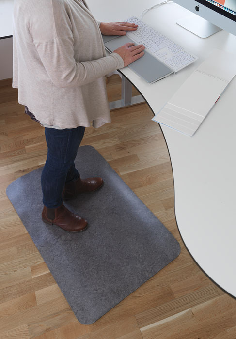 Kvinna som står på en grå Yoga Step Zedlan bredvid ett vitt skrivbord