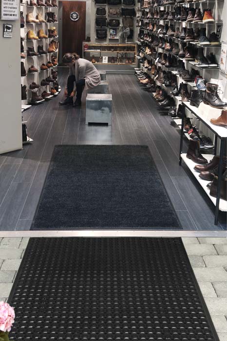 Svart skrapmatta i gummi med runda hål utanför en butik med torkmatta antracit