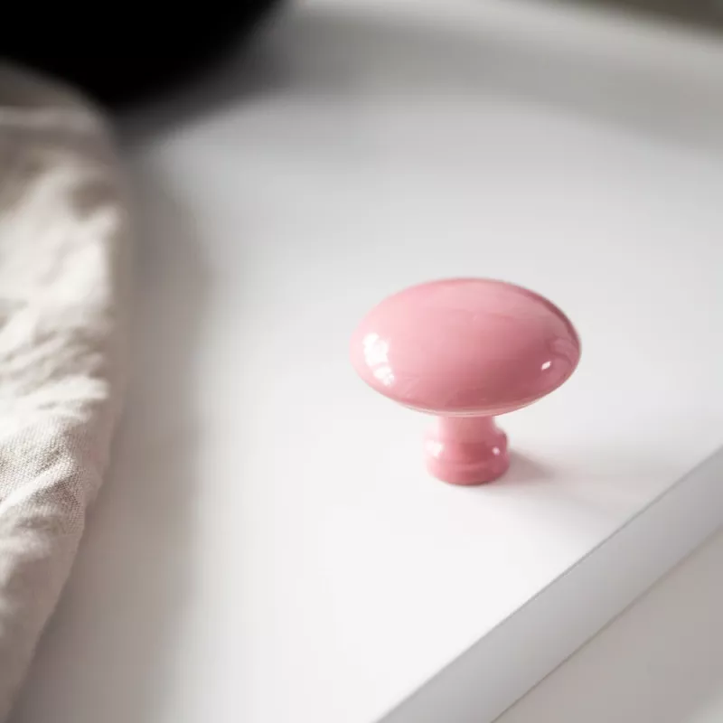 Rosa köksknopp på en vit lucka med en beige handduk bredvid.