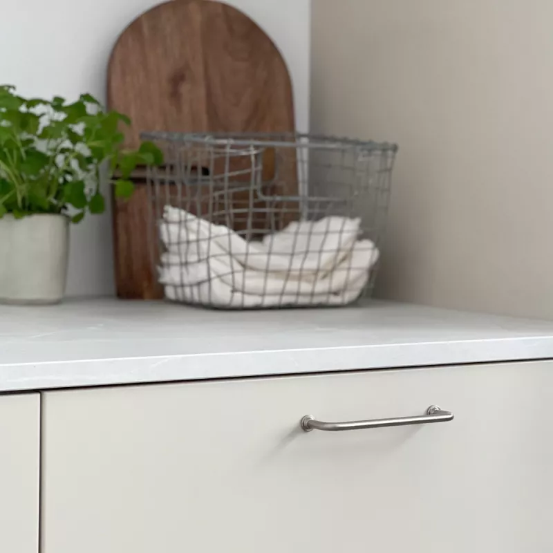 Ett rostfritt stålhandtag med en enkel och modern design, monterat på en vit kökslucka och vit marmor-bänk.