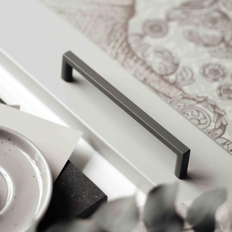 Ett grönt kökshandtag monterade på en ljus kökslucka med dekorerade tallrikar och textilier runtom.