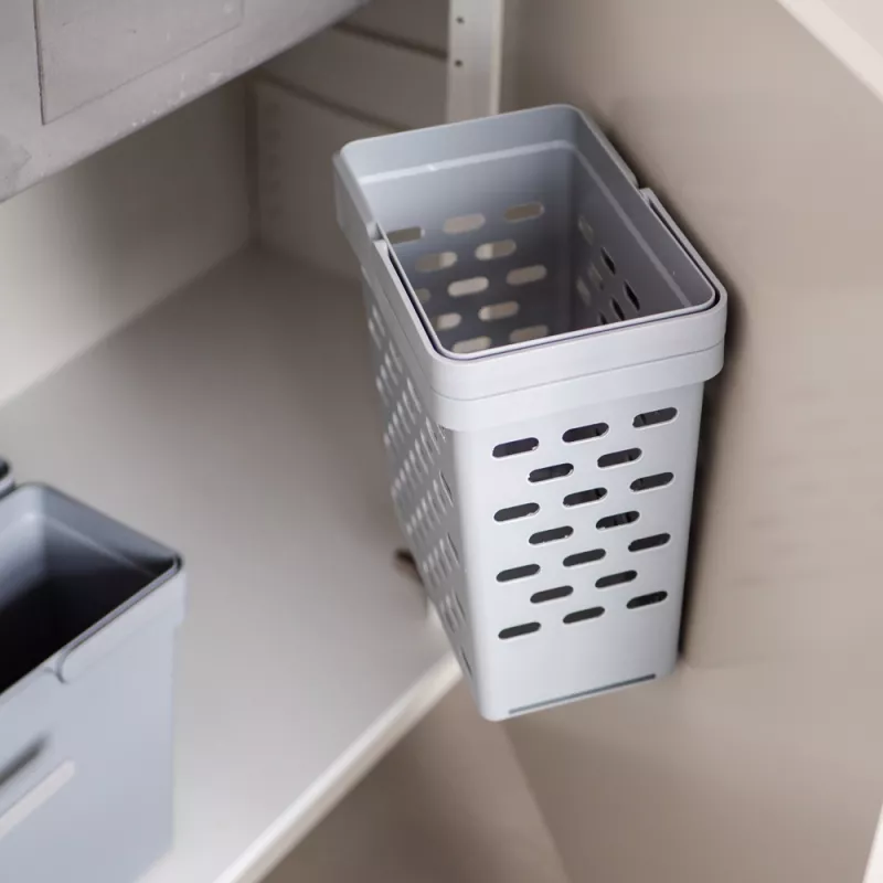 Ett grått sopsorteringskärl placerat under en diskbänk. I bakgrunden finns ett annat kärl som är monterat på en utdragbar plattform.