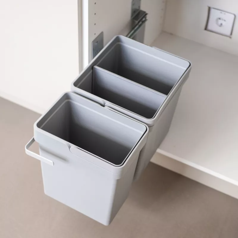 Under diskbänken finns ett grått sorteringskärl. I bakgrunden syns ett annat kärl av samma typ, monterat på en utdragbar hylla.