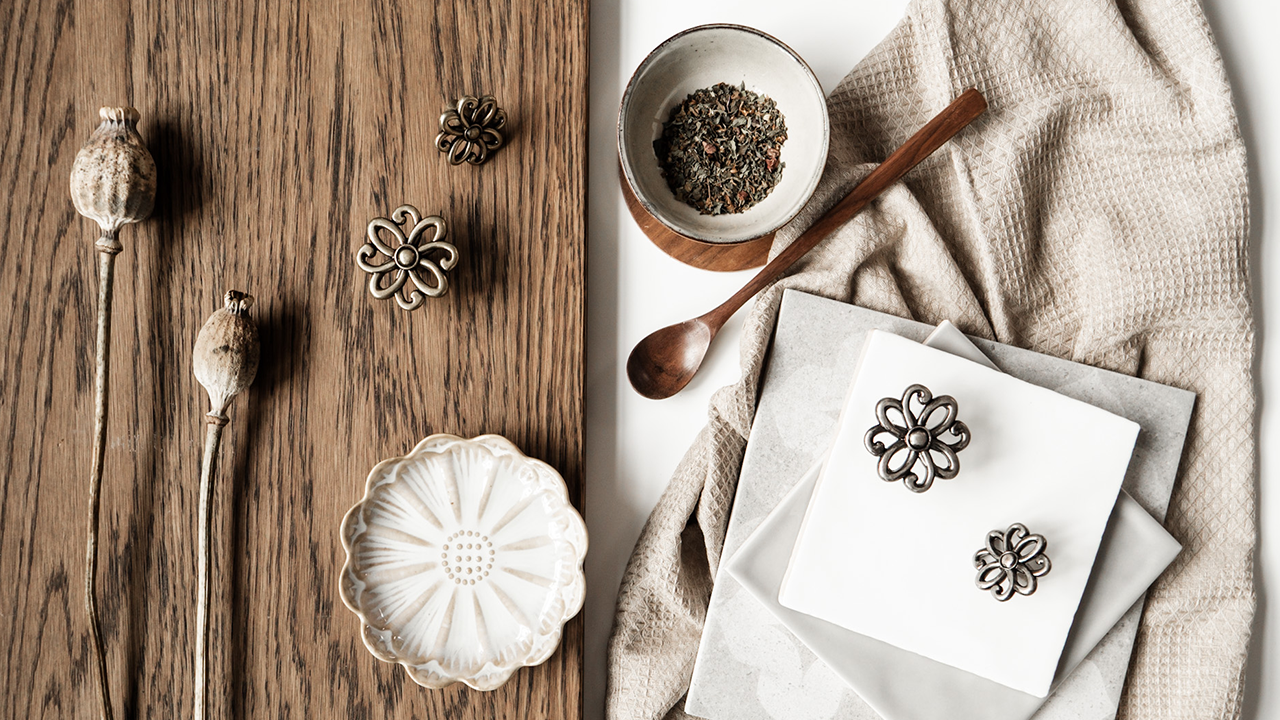 Marrakech – en rustik knop med boheme‑charme! Ett set med metallknoppar i olika storlekar, arrangerade på en träyta och en mörk skål. Bredvid ligger färgprover och en beige tygduk.