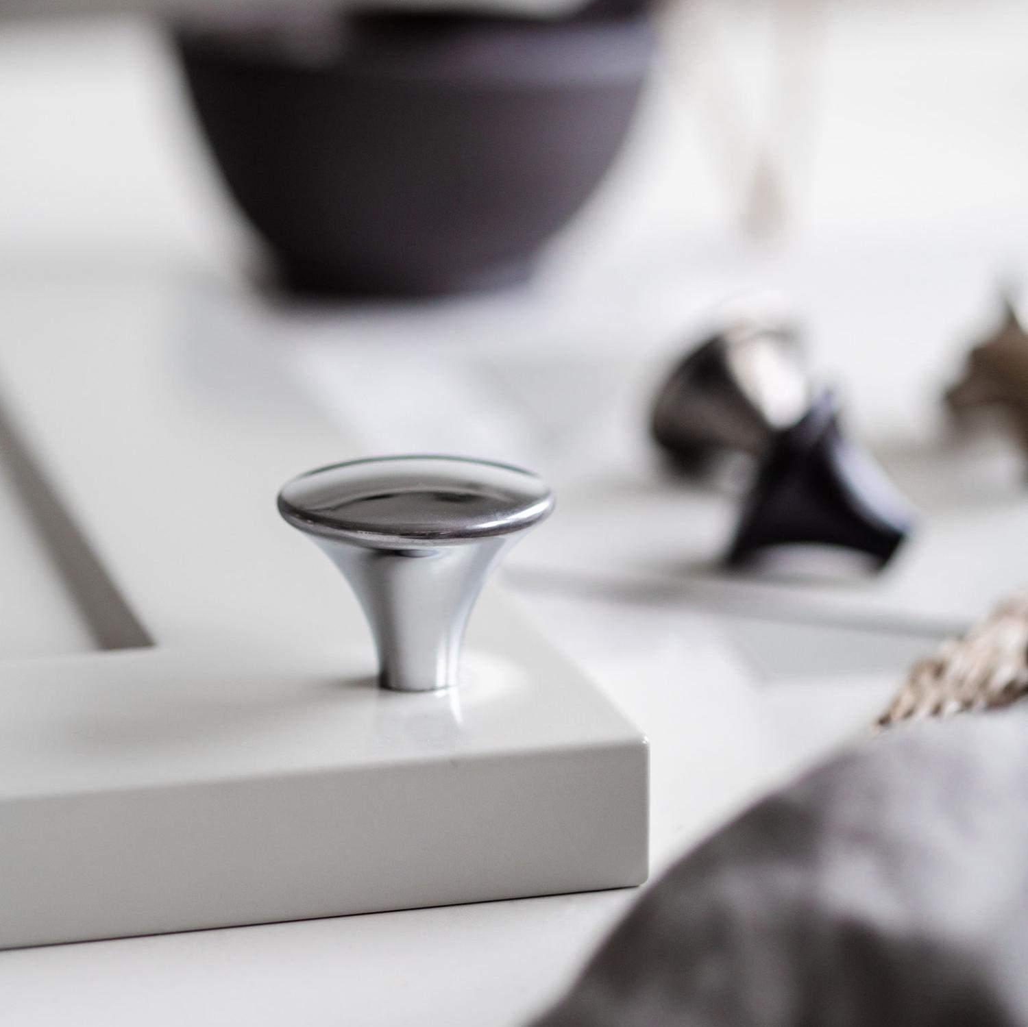 Modern kromad knopp monterad på en grå kökslucka, med suddiga knoppar i bakgrunden.