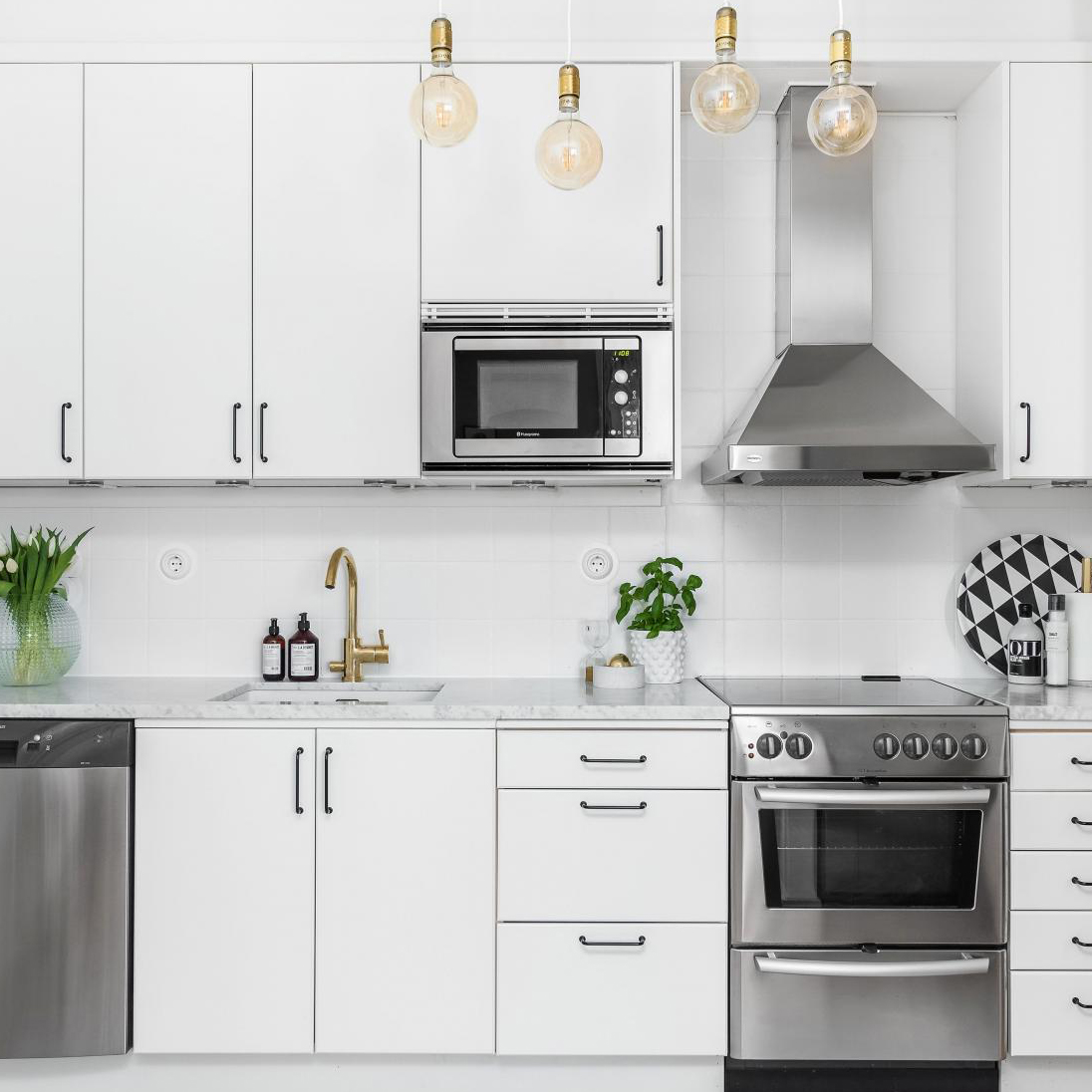 Ett modernt kök med vita skåp, svarta handtag, och rostfri ugn samt mikrovågsugn.