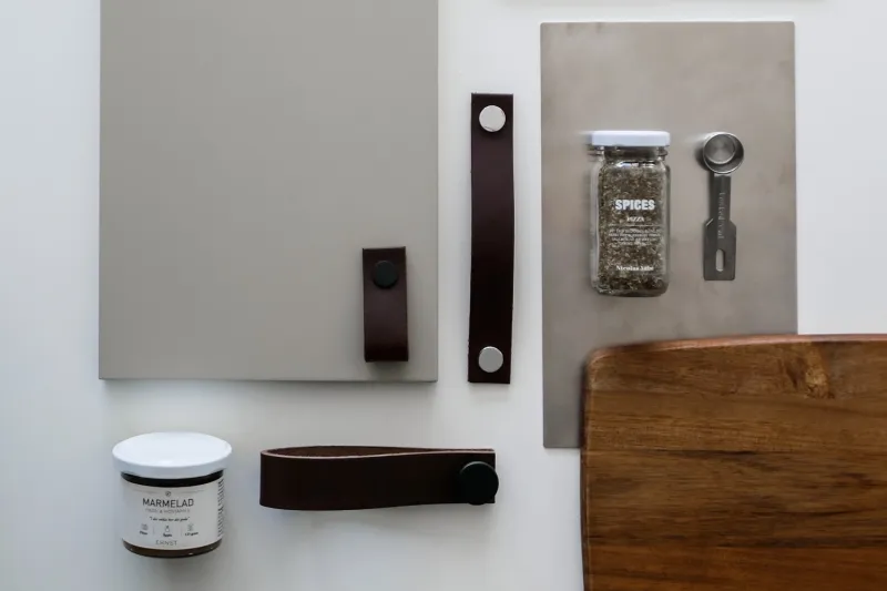 Brown leather loops and handles beside a beige kitchen front, wooden tray and spice jar