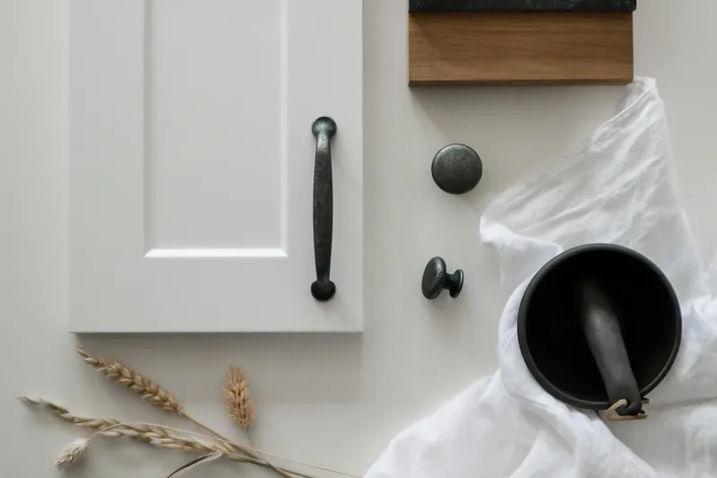 Classic white framed cabinet door with a dark rustic handle, round knobs and wood and stone samples