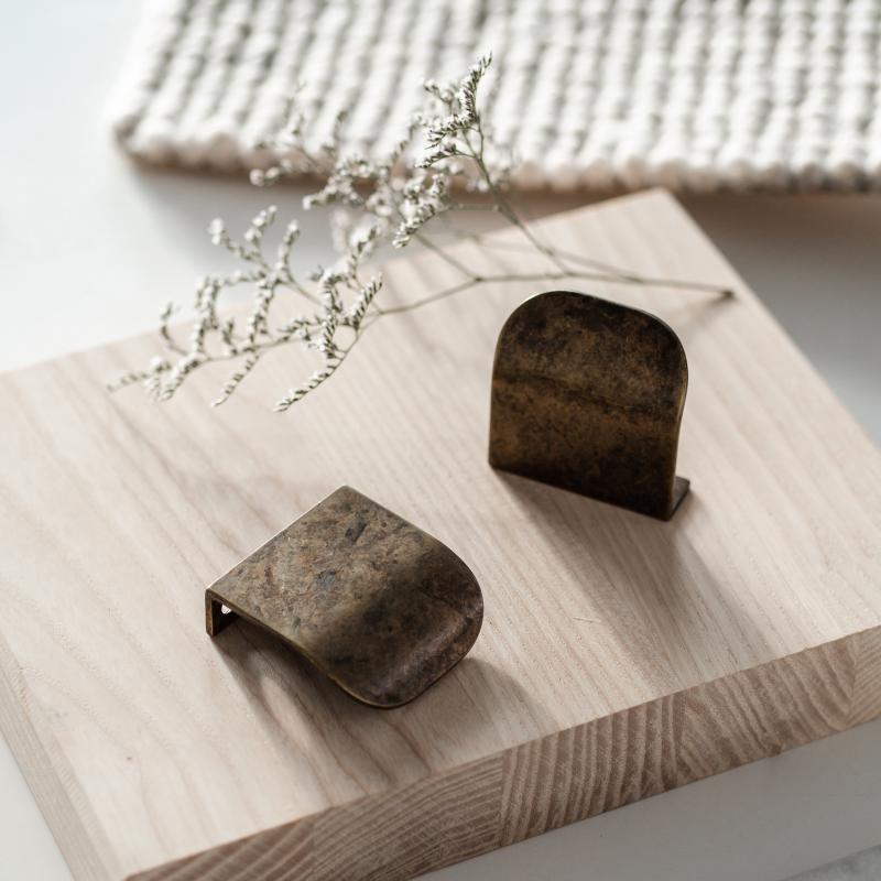 Stilleben med inspiration till köksrenovering innehållande träskriva, vita blommor och två antikfärgade profilhandtag.