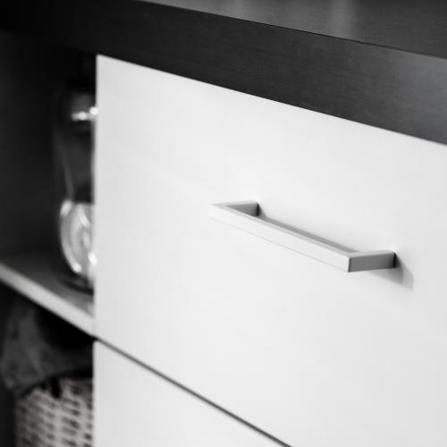 Vitt stilenrent kökshandtag mot en vit kökslucka och grå bänkskiva