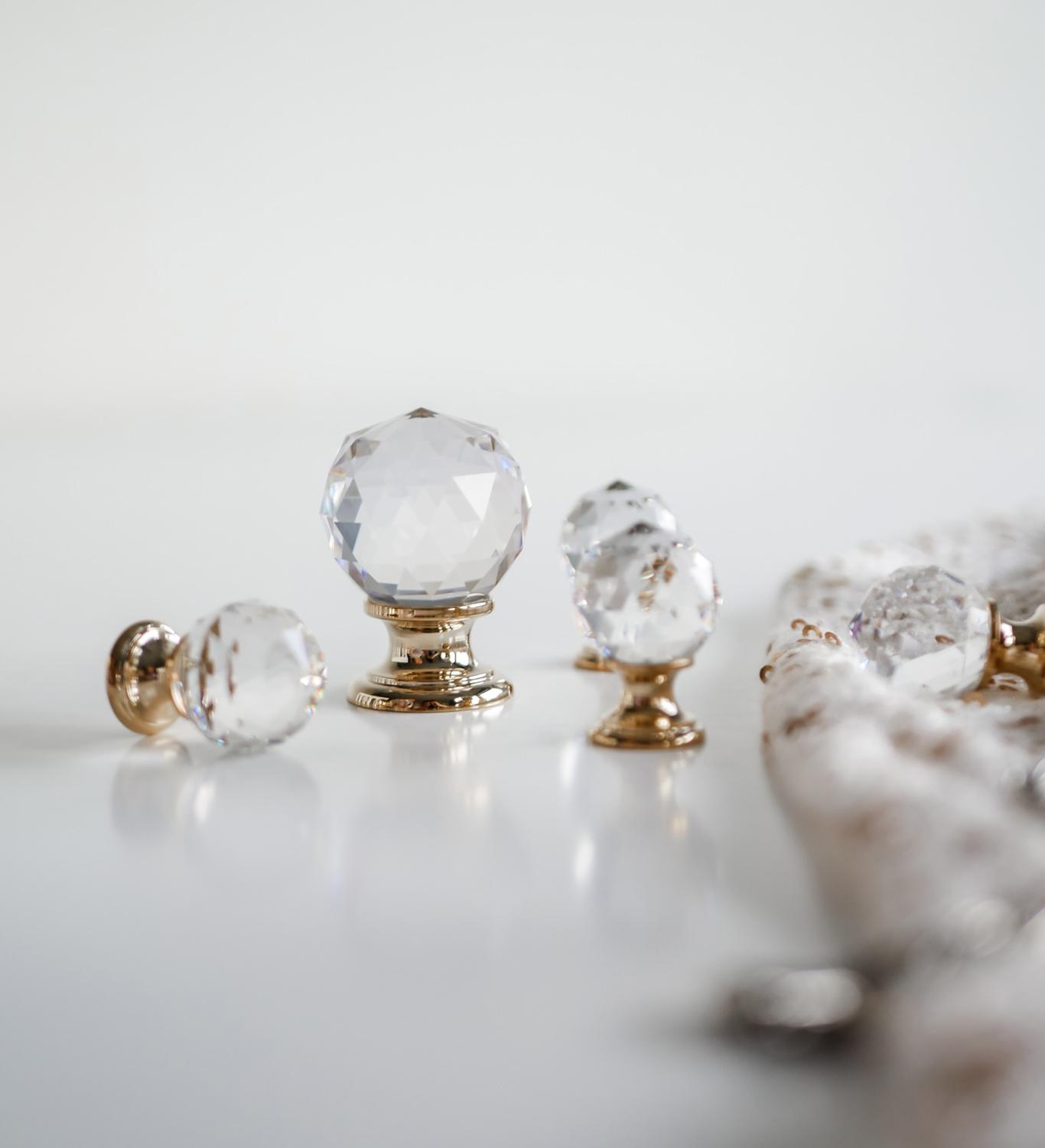 leganta köksskåpsknoppar med fasetterade kristallbollar med guldbaser, placerade på en vit yta.