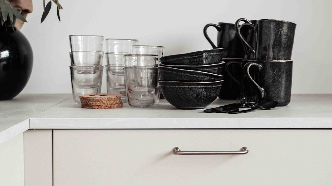 Organisera köksskåp - 4 tips på hur du kan skapa ordning i köksskåpen Svarta skålar och glas på köksbänk med ett metallhandtag synligt på skåpslådan under.