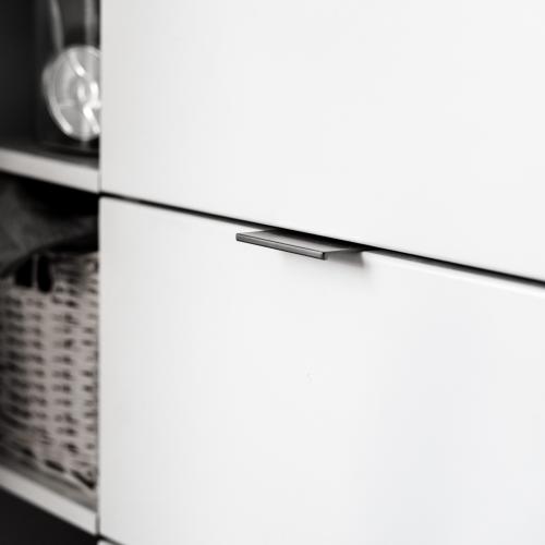 Profilhandtag i matt nickel mot vit lucka och grå bänkskiva.