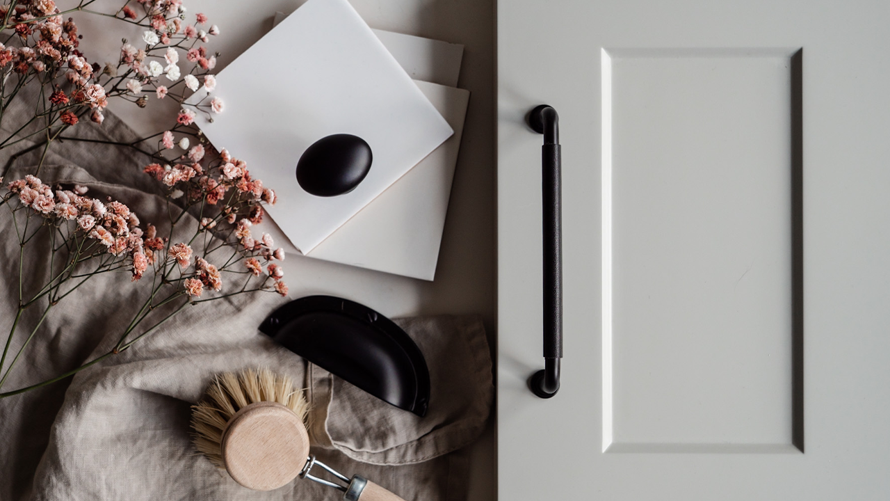 Renovera smart. Enkla tips för att uppdatera ditt kök. Svarta handtag mot grå bänkskiva och en hög med prover. Bredvid ligger en diskborste i trä och en bukett med rosa blommor.