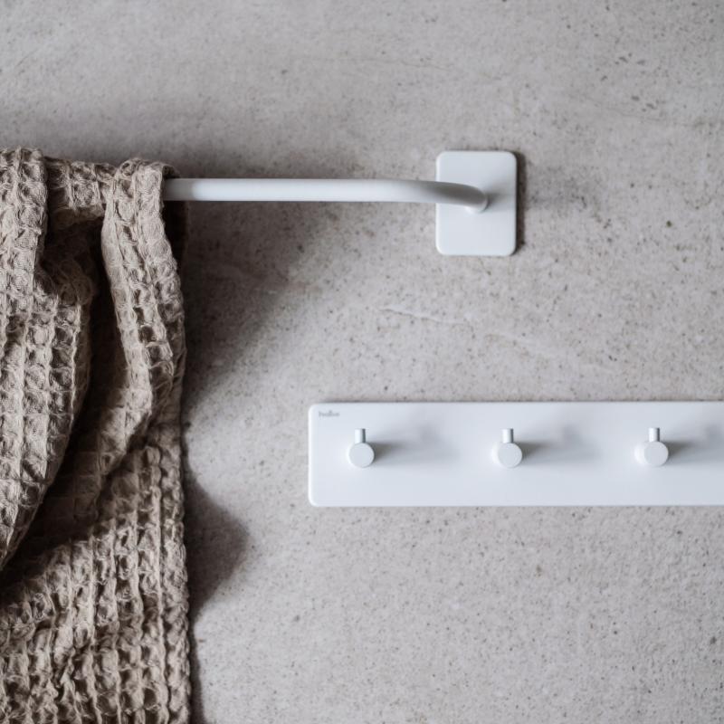 Handdukshängare i vitt och krokrad i vitt mot en beige bakgrund och en beige handduk.