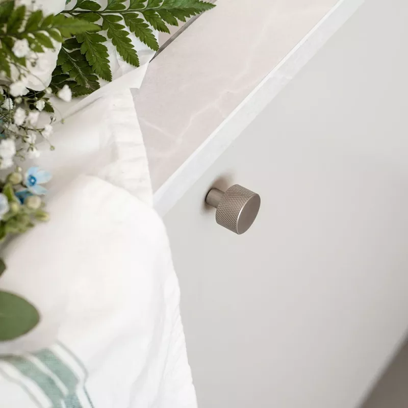 Borstad nickelknopp och handtag på en beige skåplucka, dekorerad med gröna blad och färgprover.