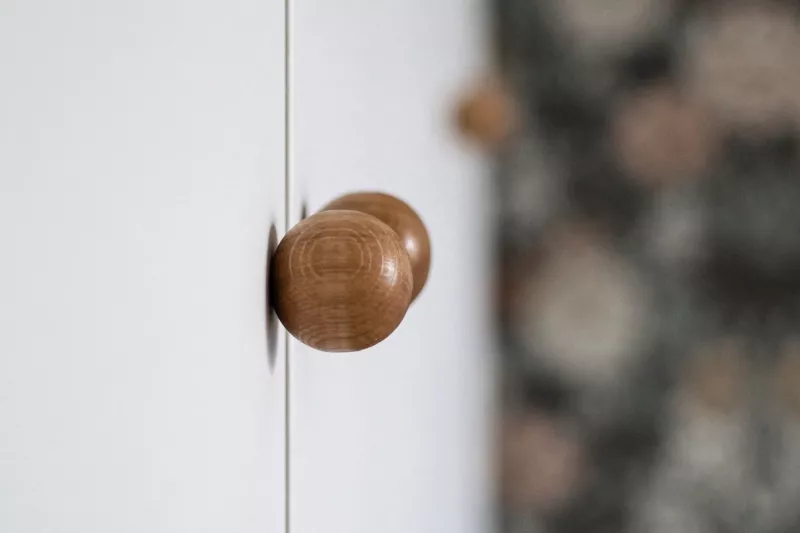 Rund träknopp på vit skåpdörr med blommig tapet