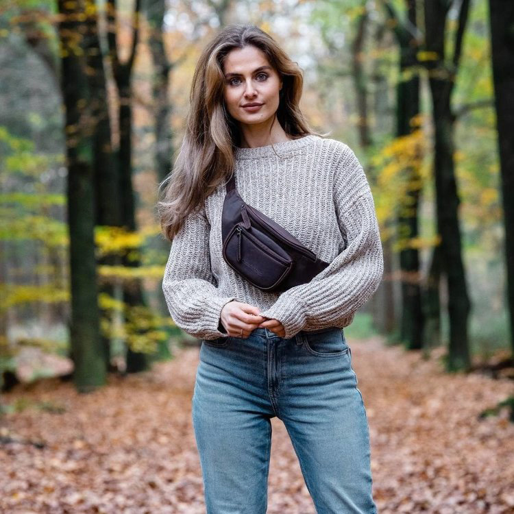 kvinna som står i lövskog på hösten och har en svart midjeväska i läder av modellen jack från varumärket the  chesterfield brand