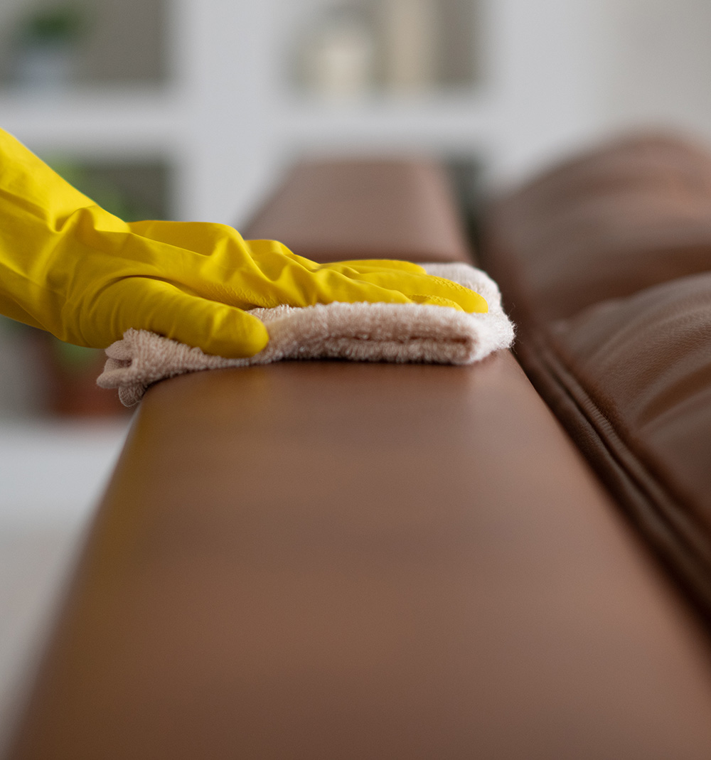 gummiklädd hand som torkar av en soffa med en rengöringsduk